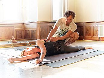 Yogalehrer, Typberatung nach Ayurveda, Thai Vedic, Dosha Test, Ernährung Coach, Ernährung nach den 5 Elementen, Ayurveda, ayurvedische Ernährung Routine, Thai Yoga Massage, Thaiyogamassage, Yogakurs, Yoga Klassen, Yoga Personal Training. Massage als Anwendung von einem Mann an einer Frau bei der Yoga Therapie gegen Schmerzen und Rückenproblemen bei einer Thai Yoga Massage und Yoga mit Ayurveda als Kur.