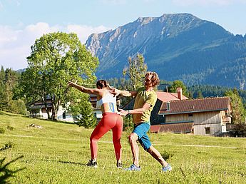 Rückenschmerzen Training, Wirbelsäule, Rückentraining, Schmerztherapie, L 4/5 und Lendenwirbelsäule L 3/4 Ein Mann in den Allgäuer Alpen als Personal Trainer beim trainieren mit einer Frau in der Natur bei outdoor Aktivität an Physio Übungen für Schmerz, Therapie, Linderung und Gesundheit bei gutem Wetter.