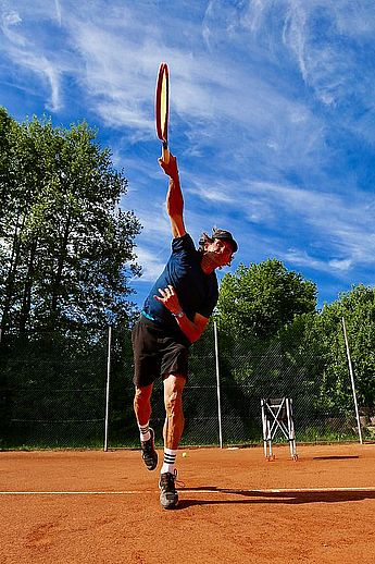 Tennistrainer, Tenniskurse, Tennisschule, Tennistraining für Kids, Kinder und Jugendliche, Tennis Camps, Vereine, Mannschaftstraining, Einzeltraining, Gruppenkurse, BTV Trainer B-Lizenz Wettkampf in Kempten und im gesamten Allgäu. Ein Mann beim Aufschlag im Tennis auf dem Spielfeld mit einem Schüler zum Tennistraining.